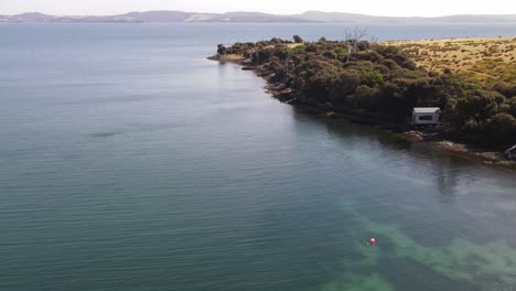 Drone-aerial-move-forward-past-beach-house-over-tropical-blue-water-around-nature-and-mountains