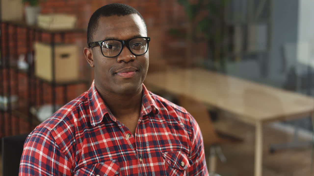 Portrait Of The Young Handsome Man In Glasses And Red Motley Shirt Sitting In Front Of The Camera And Smiling