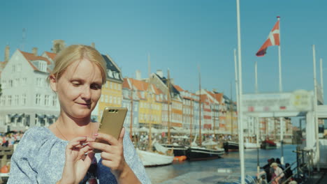 Eine-Glückliche-Frau-Benutzt-Ein-Smartphone-Steht-Vor-Dem-Hintergrund-Des-Kanals-Und-Der-Beliebten-Touristenstraße