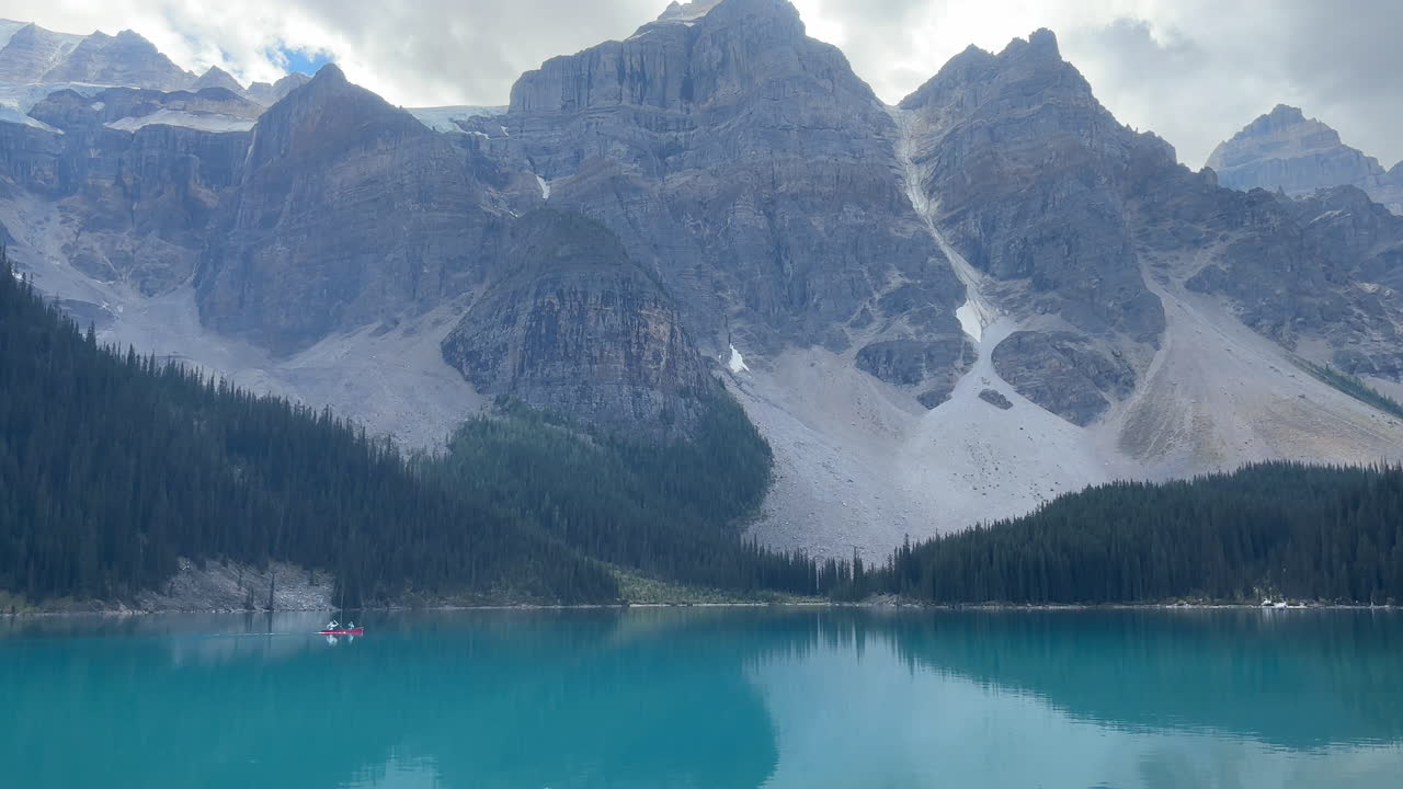 Mountain landscape, people rowing small boat on turquoise water lake. Handheld