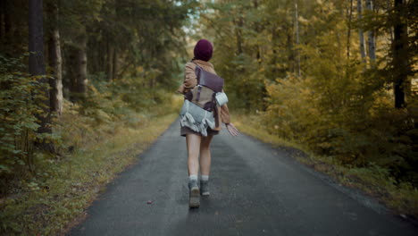 female tourist with backpack running on road by forest