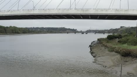moscas aéreas bajas bajo el puente de cable en el río fangoso suir en irlanda