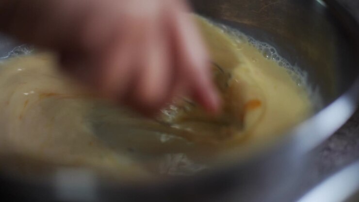 Egg yolk and milk whisked and blended in metal bowl, filmed as closeup slow motion shot