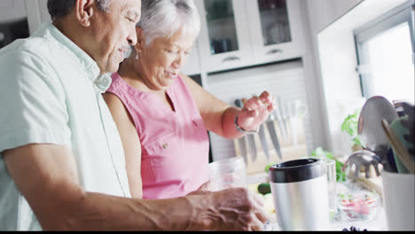 Happy-senior-biracial-couple-preparing-healthy-drink-in-kitchen