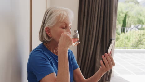 senior woman enjoying tea while video chatting on smartphone at home