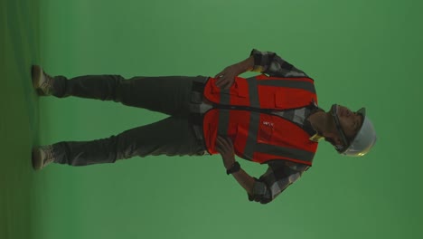 full body of asian male engineer wearing safety helmet looking around while standing with arms akimbo in the green screen background studio, during sunset or sunrise time