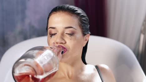 young woman with flowed mascara in the milk bath looking in the camera and drinking sparkling wine from the bottle feeling