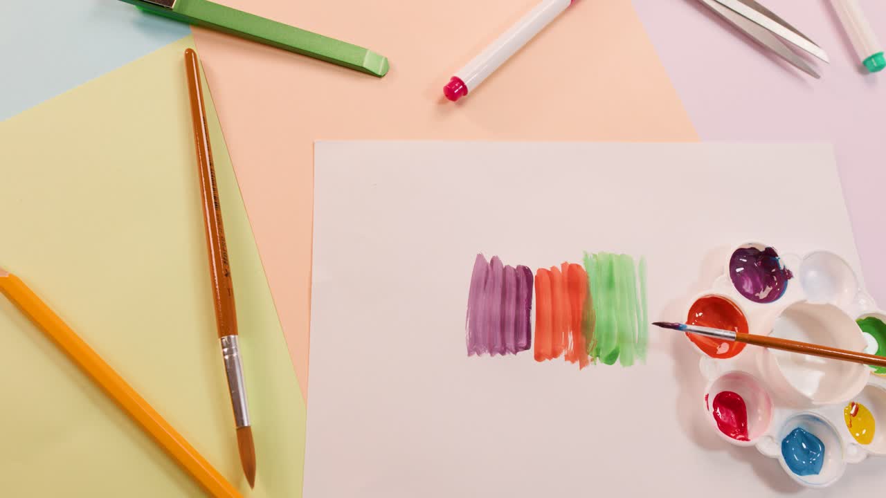 Overhead view of hand painting vibrant acrylic stripes on white paper, surrounded by art supplies