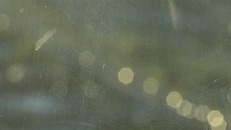 artistic six-sided bokeh of car lights gleam out of focus on a dirty glass window creating a golden green abstract experience