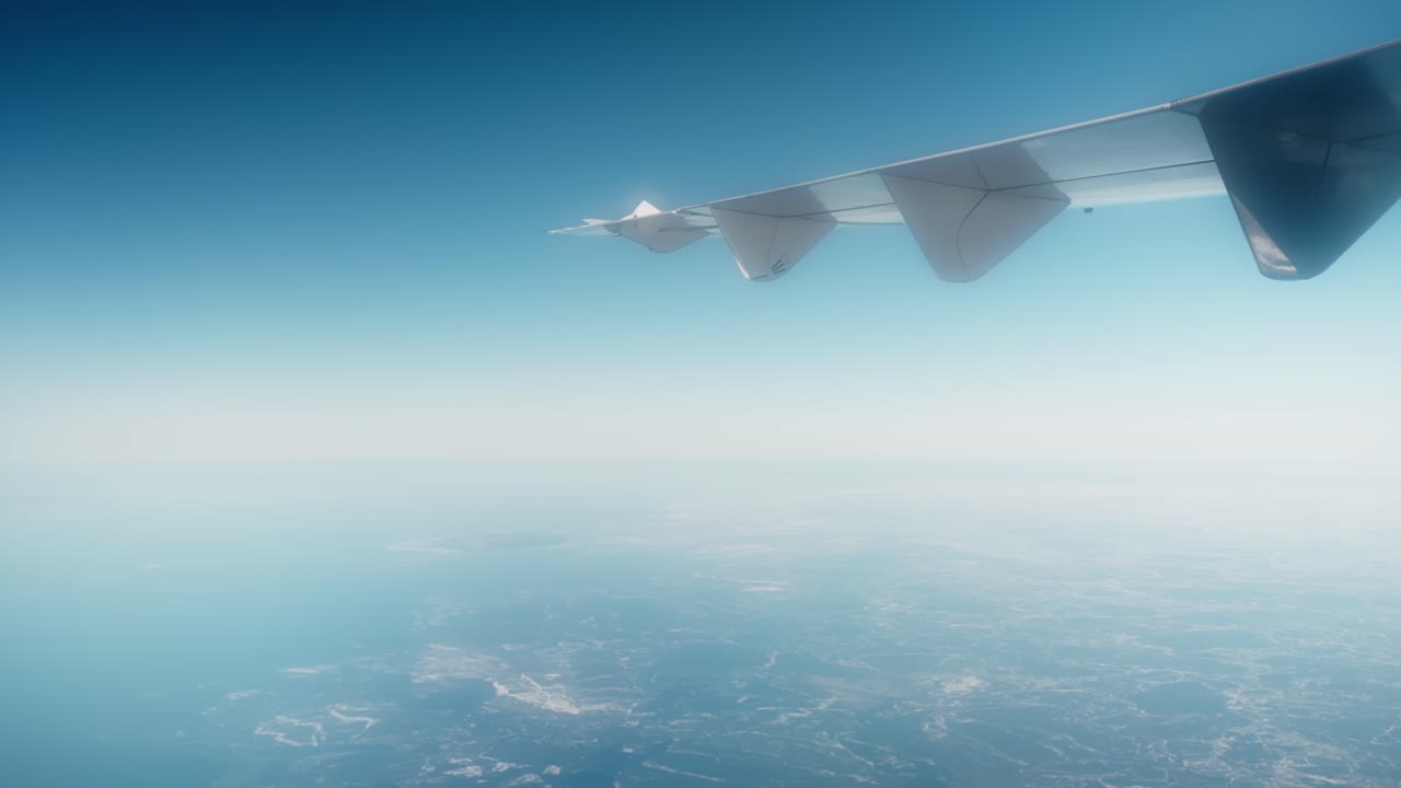 淡い青い霞がかかったフィンランド上空を飛ぶ飛行機の翼。かすかな海岸線と凍てつく北欧の風景の上空を、柔らかな霧の雰囲気の中で高高度飛行を捉えた一枚。