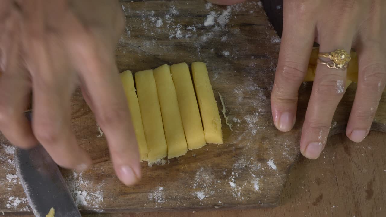 mujer chef mano cortar la masa de galletas en cuadrados en la tabla de corte de madera vista superior
