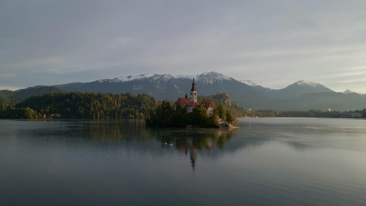 Isola del Lago di Bled con Chiesa e Montagne Innevate all'alba.