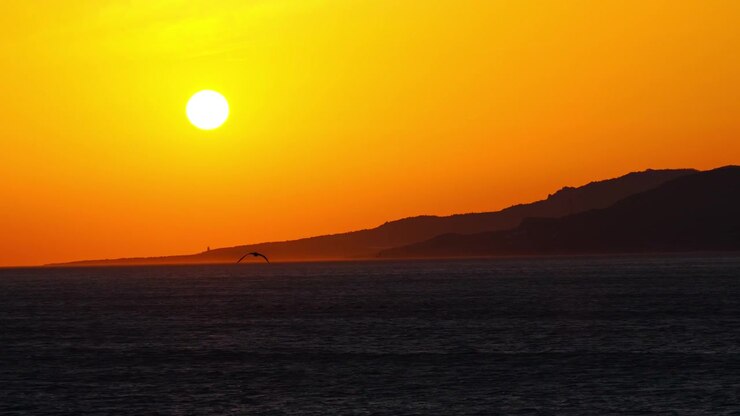 Pôr do sol cinematográfico sobre a Praia de Los Lances em Tarifa, Espanha. A luz dourada quente ilumina a costa atlântica, criando uma atmosfera costeira épica e um cenário noturno inesquecível