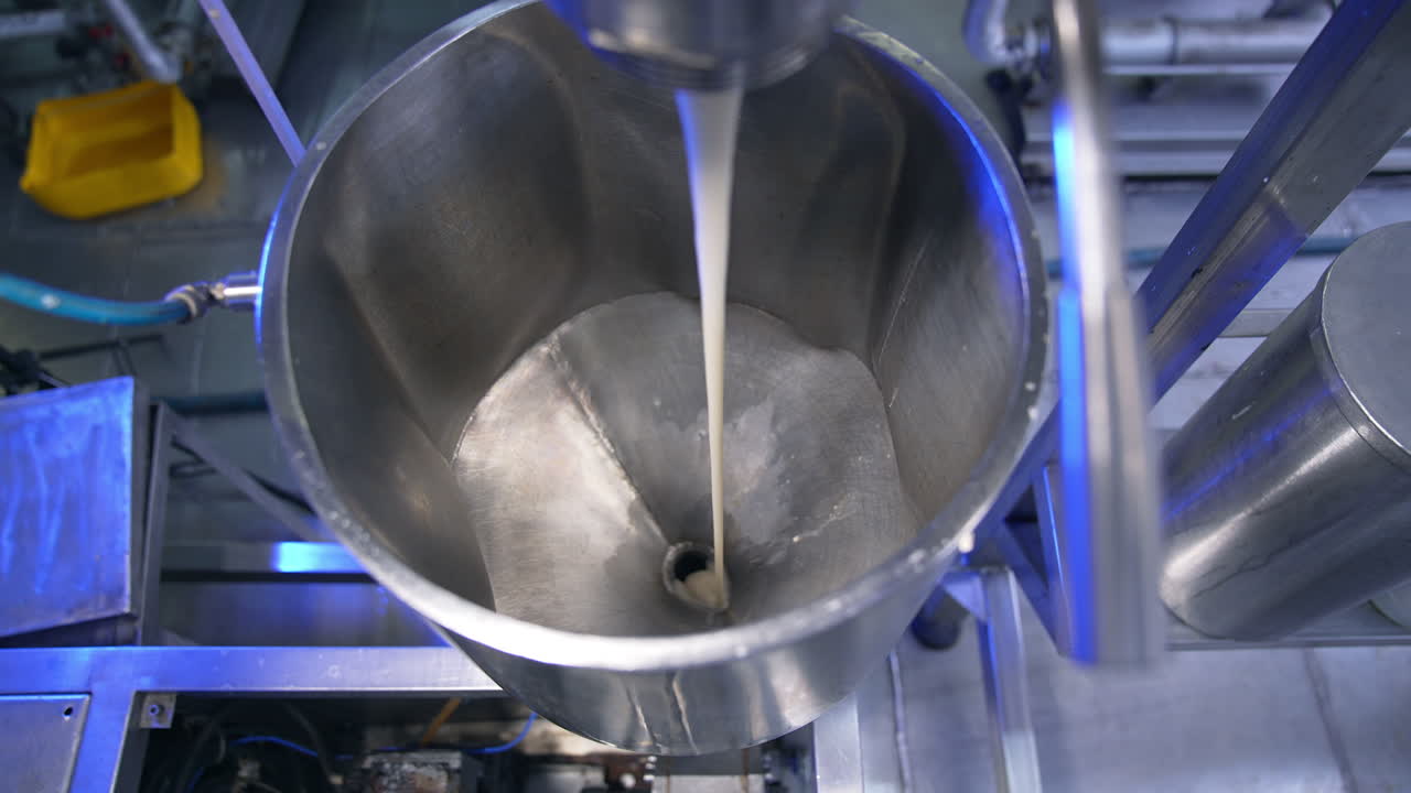 Condensed milk streaming from a tube into a metal container. Close up. Food factory automated line. View from above.