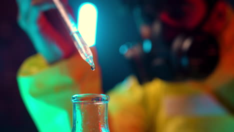 primer plano de la pipeta química que deja caer líquido transparente en los tubos de laboratorio con un químico científico borroso que usa una máscara respiratoria en segundo plano