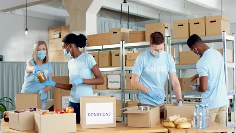 multiethnic group of volunteers in facial mask packing boxes with food and water in charity warehouse