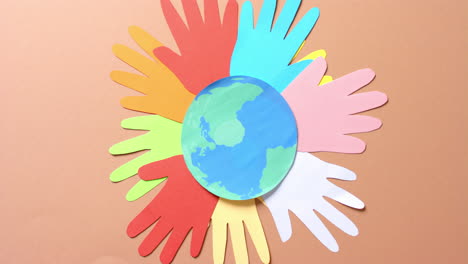 close-up van handen samen met een globe gemaakt van kleurrijk papier op bruine achtergrond met kopieerruimte