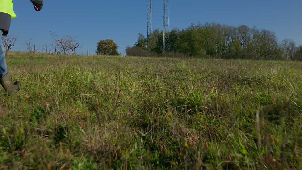 trabajador caminando por la hierba hacia las dos torres celulares, bajo ángulo de inclinación disparo revelando