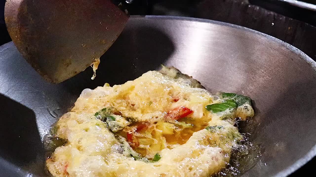 Un primo piano dettagliato di una frittata soffice con verdure che cuoce in un wok di metallo