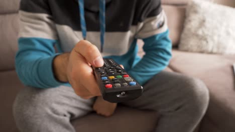 hombre en el sofá hojeando canales de televisión con control remoto en la mano