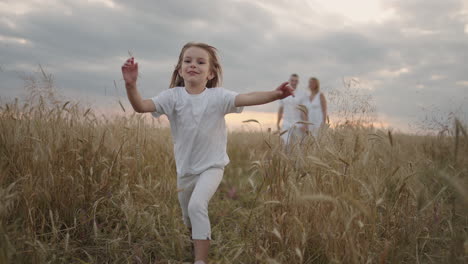 a happy smiling little girl looking at the camera runs in slow motion at sunset in a field of grain ears