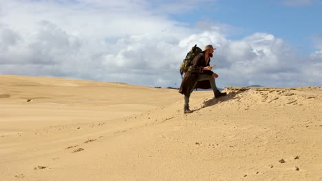 Un-Excursionista-Que-Lleva-Una-Mochila-Mira-Los-Patrones-De-Arena-En-Dunas-De-Arena-épicas