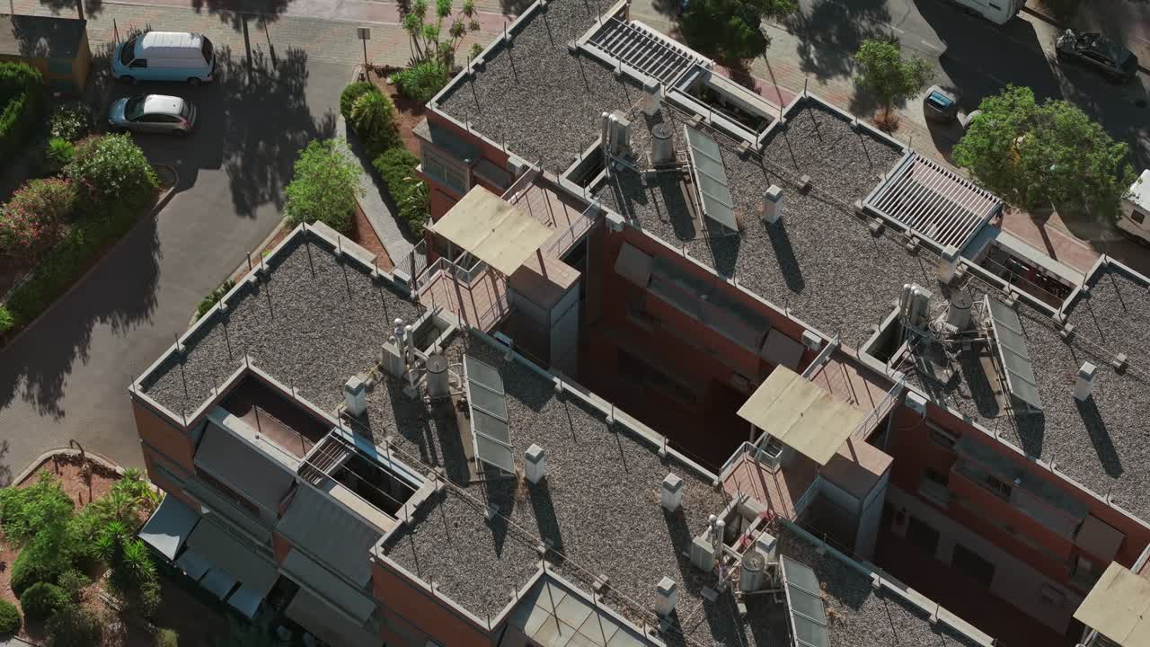 A top-down aerial view captures an urban residential block, highlighting rooftop installations, solar panels, green courtyards, and parked vehicles, ideal for themes of urban living, architecture