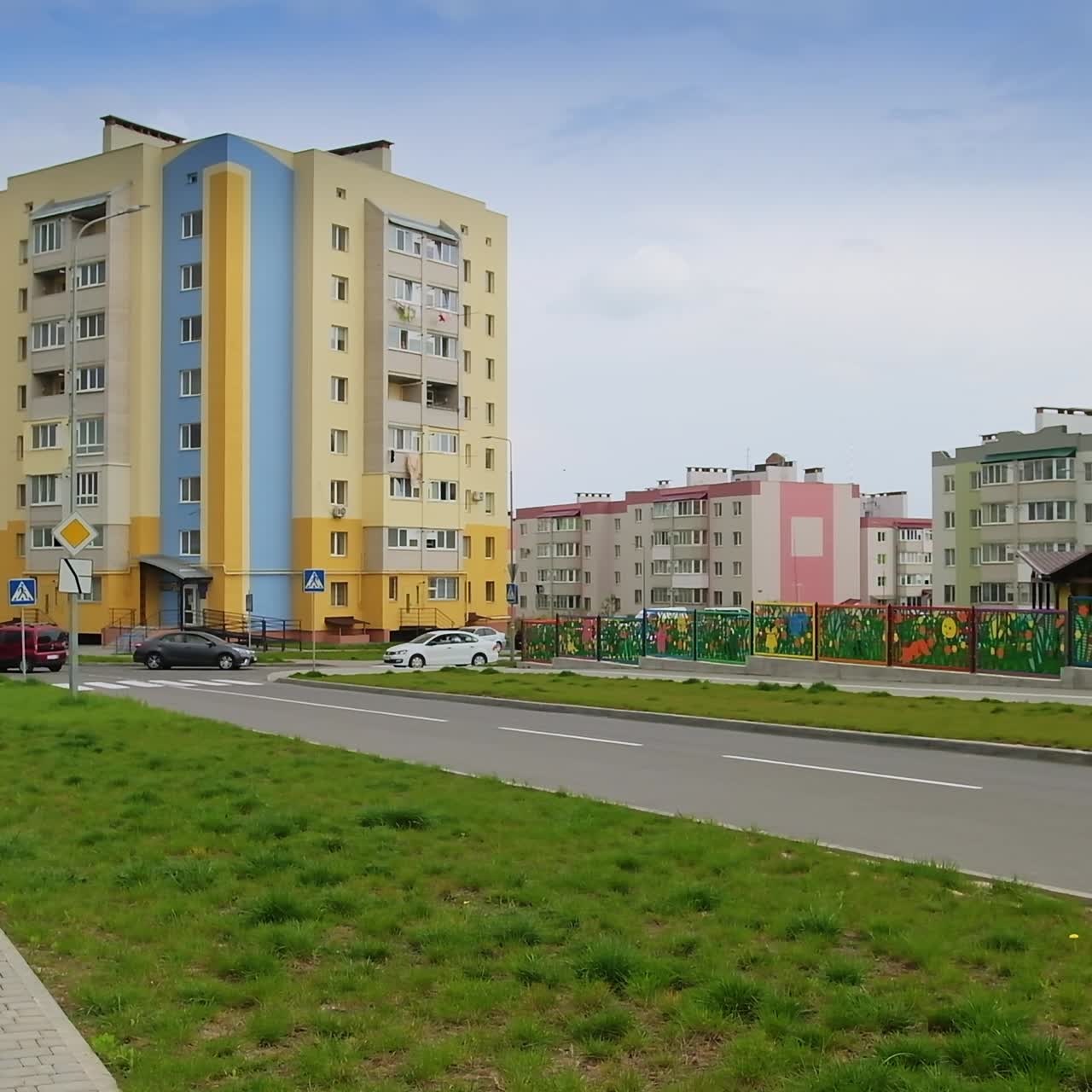Beautiful cozy residential area with new recently built multi-storied buildings. Cars move by the roads. Pavement with green lawn