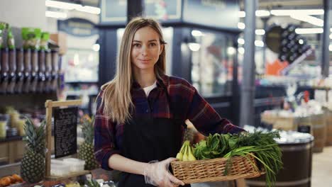 supermarktangestellte in schwarzer schürze, die eine kiste voller obst und gemüse im supermarkt hält