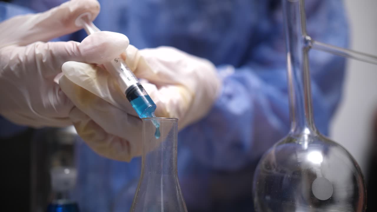 Scientifique transférant un liquide bleu avec une seringue dans une fiole en laboratoire