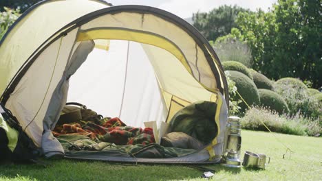 tienda de campaña amarilla con mantas y almohadas sobre los árboles en un jardín soleado