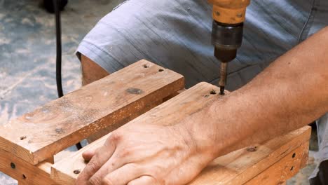 carpintero hábil que emplea un taladro eléctrico para colocar tornillos en una pequeña silla de madera en su pequeño taller para vender y apoyar la economía local
