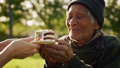 in a bright park during the afternoon, an elderly man beams with happiness as he receives a birthday cake from a caring individual. the joyful moment highlights connection and celebration.