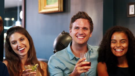 portrait of young friends meeting for drinks in cocktail bar and making a toast