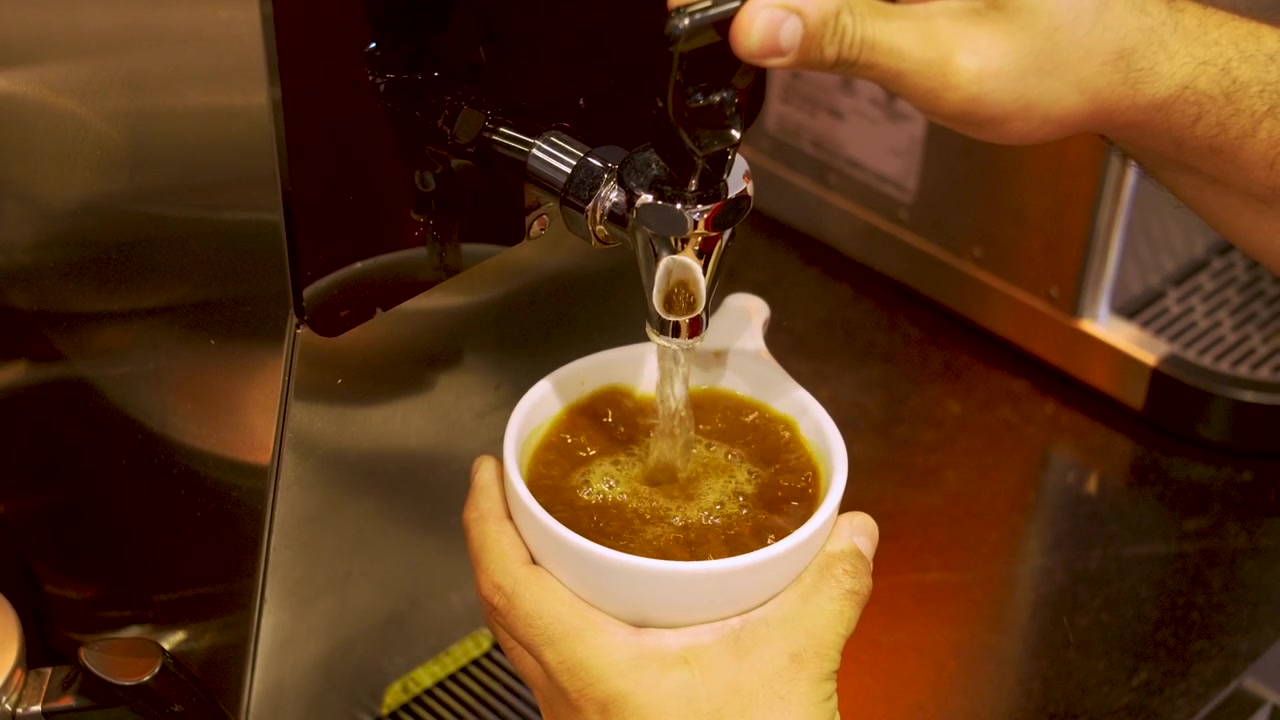 Mani del barista che tengono una tazza sotto l'erogatore di acqua calda per preparare un caffè Americano con una macchina da caffè espresso professionale.