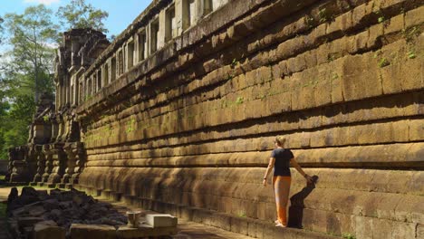 young caucasian woman walking along side of ta keo temple in the angkor wat complex, siem reap, cambodia