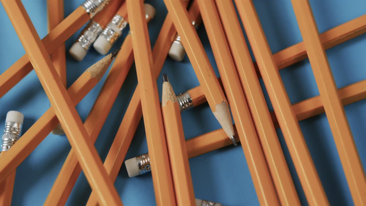 Orange pencils are scattered across a blue background, some broken with exposed graphite