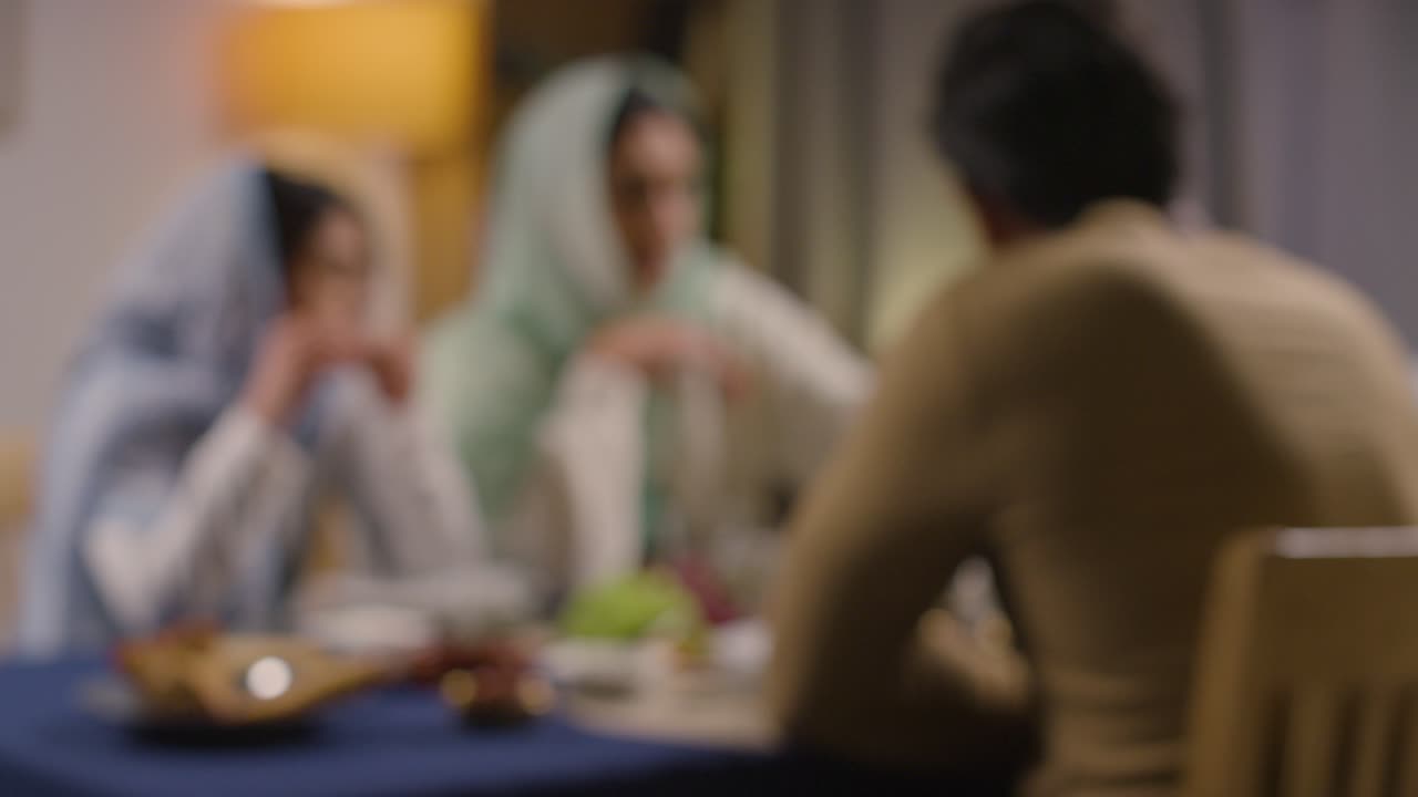 imagen desenfocada de una familia musulmana sentada alrededor de una mesa en casa comiendo juntos