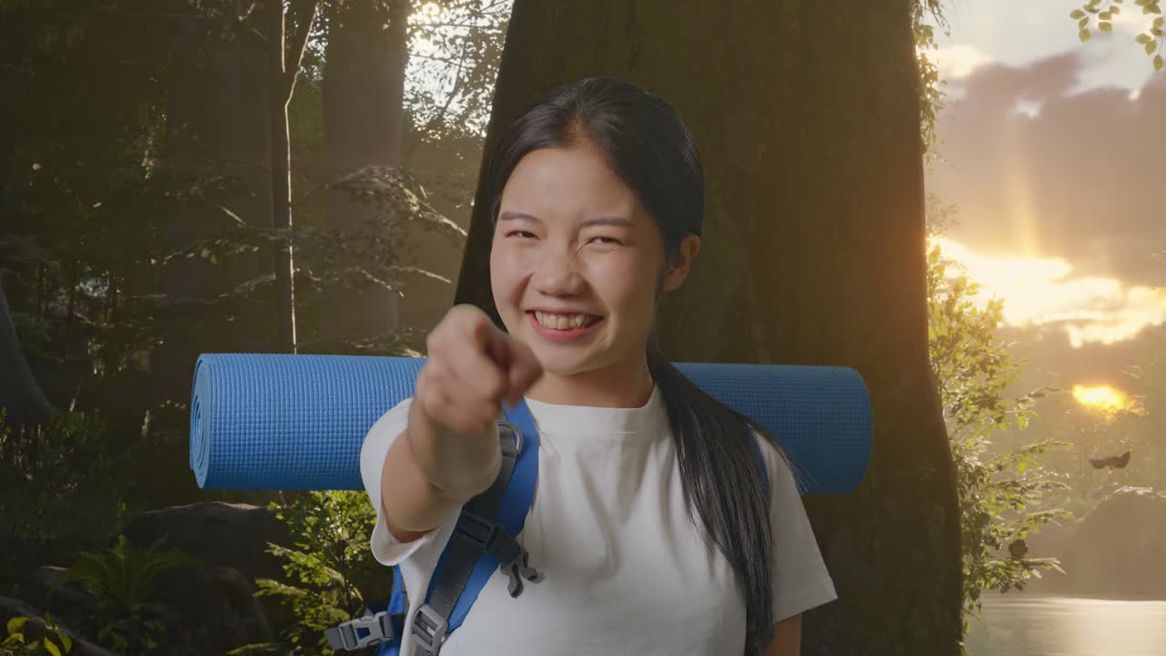 산악 배을 들고 있는 아시아 여성 하이커가 웃으며 가을 만지고 숲의 자연을 탐험하는 동안 카메라를 가리키고 있습니다.