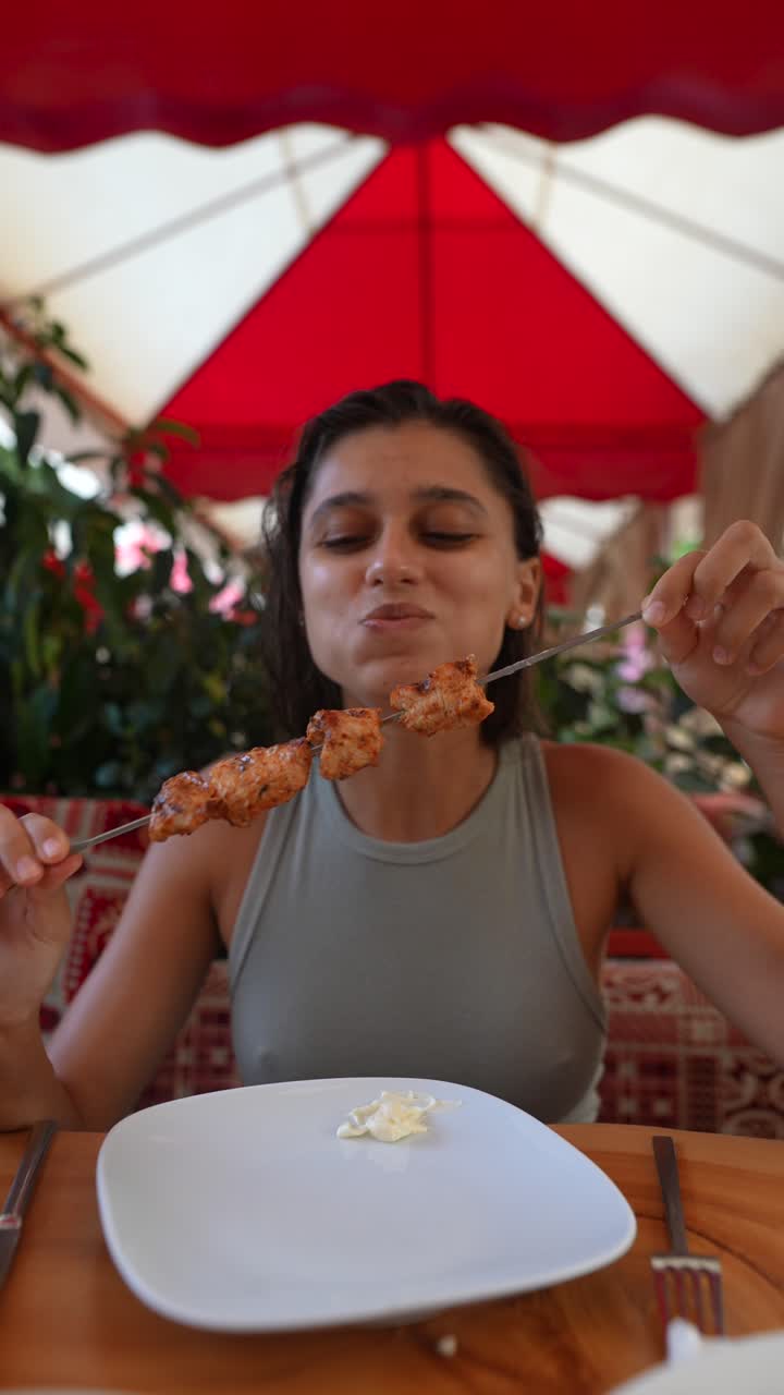 una mujer disfrutando de salchichas de pollo a la parrilla en un restaurante turco.