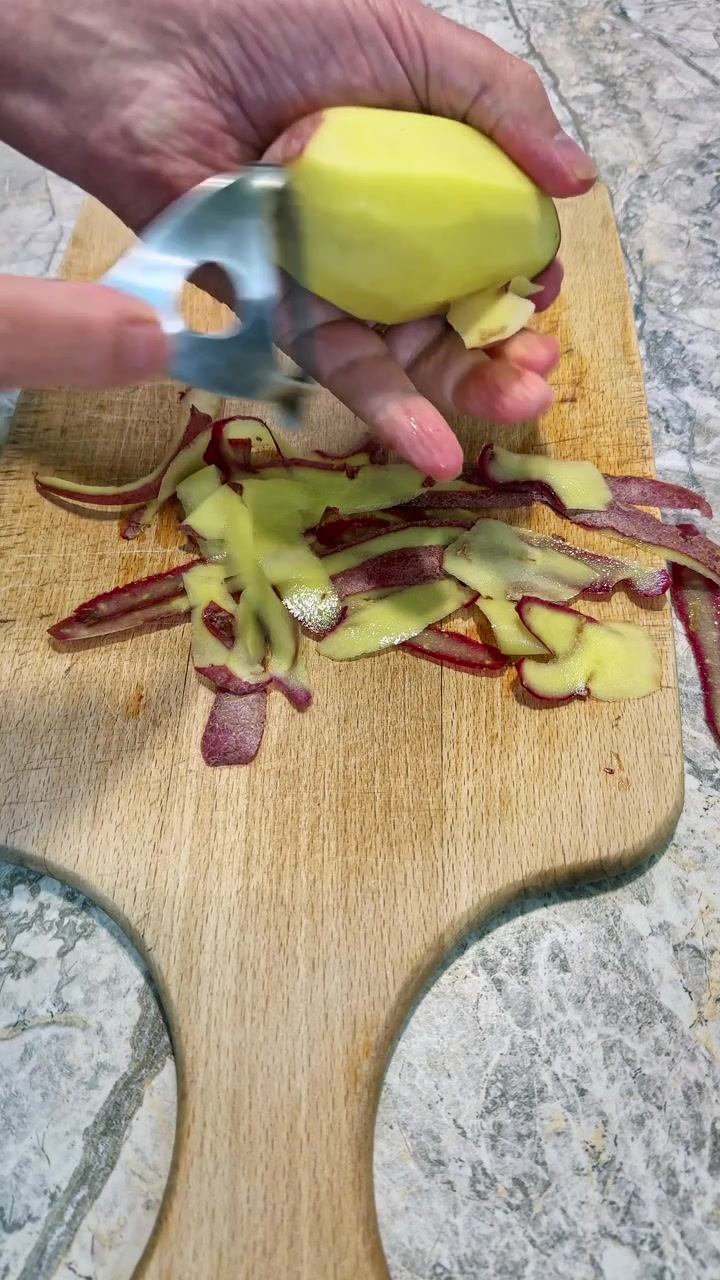 Close-up of a person peeling a fresh red potato using a vegetable peeler. Vertical 4K food preparation footage ideal for cooking tutorials and recipe videos.
