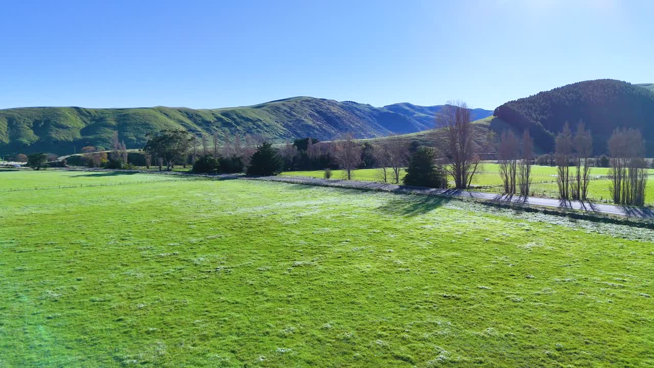 Aerial view of lush green fields and distant hills under clear blue skies in Akaroa, New Zealand