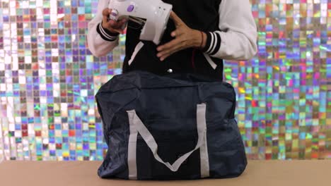 person places sewing machine inside large blue travel bag against colorful background