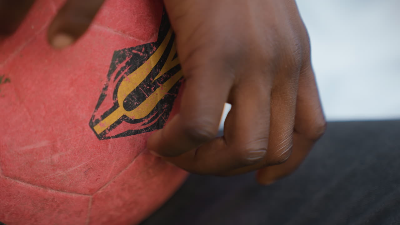 Closeup hand near red ball emblem, confident touch from player on bench, logo detail and textured rubber surface, steady fingers preparing for play with poised control and intent