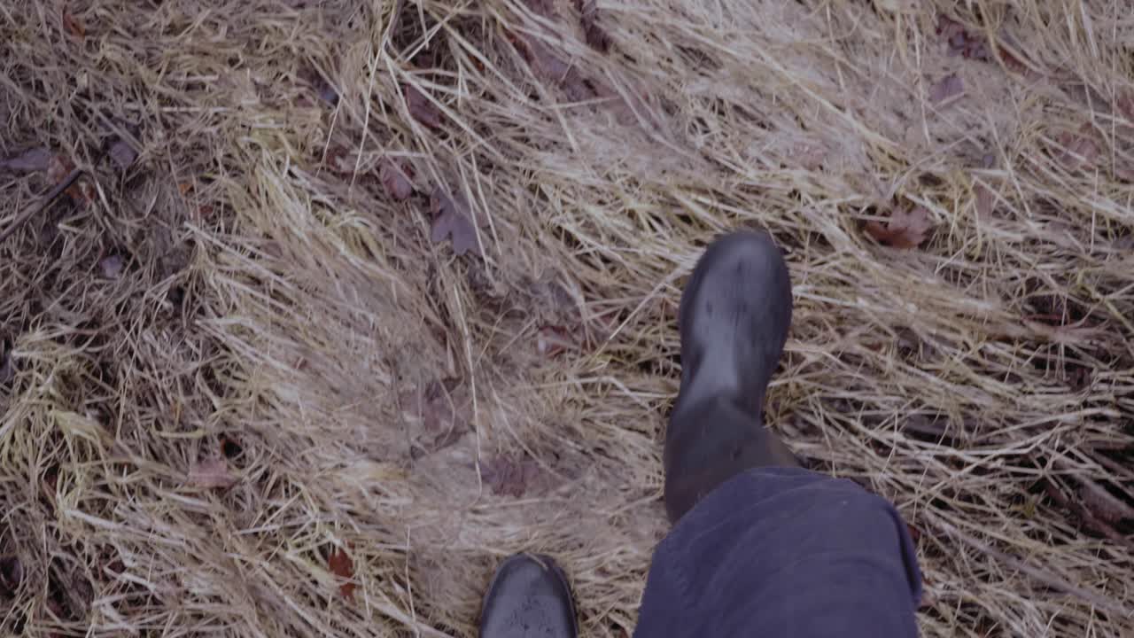 Man in wellies walking through muddy wet field puddles, slow motion point of view