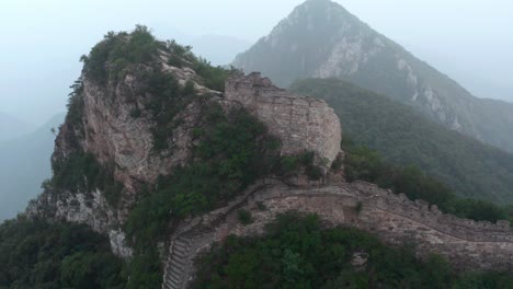 old deteriorated square lookout tower of great wall of china on top of mountain summit on a cloudy day