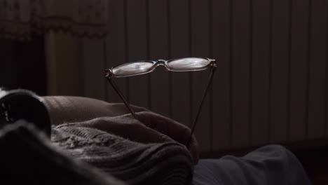 Old-man-in-sweater-holds-glasses-in-his-hand-as-he-falls-asleep-breathing-deep-DETAIL