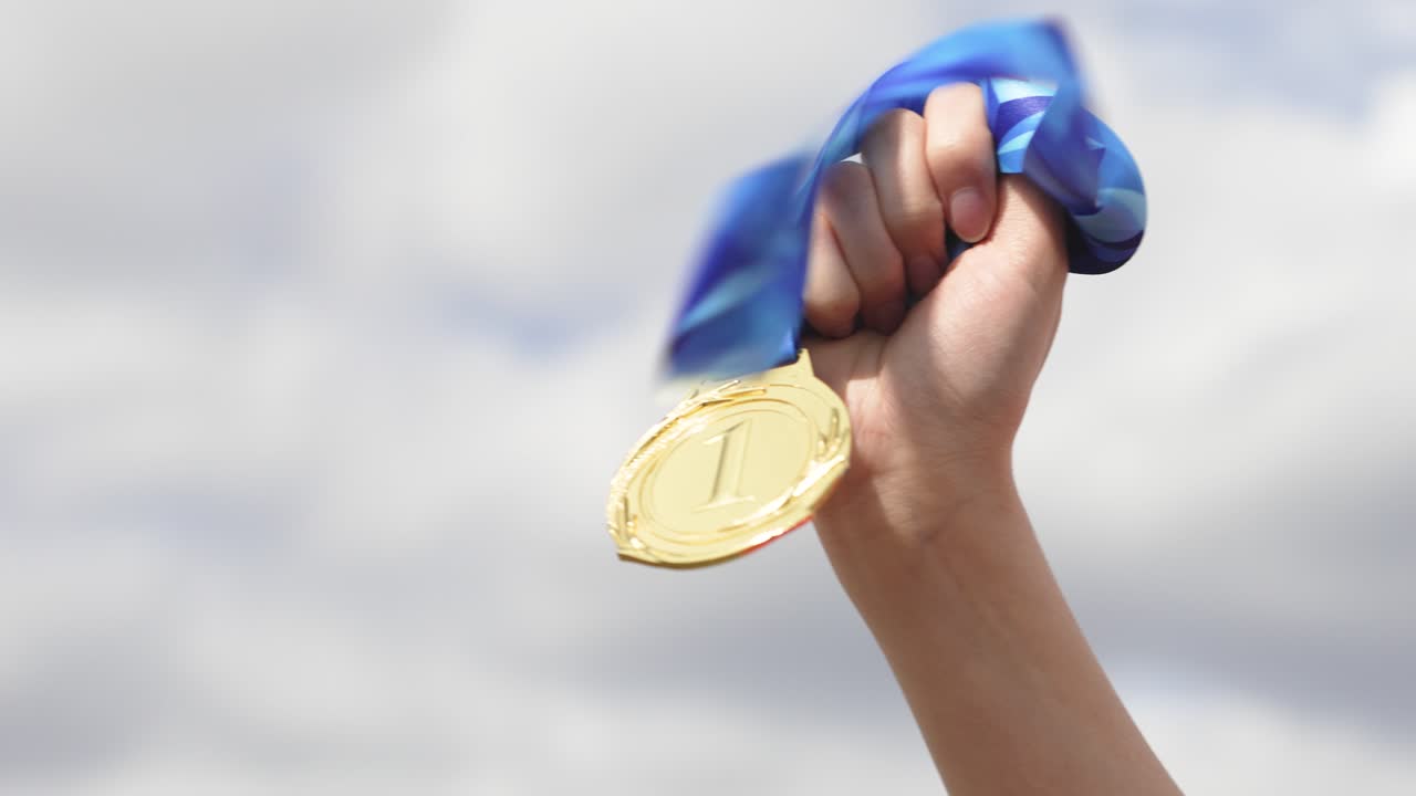 Hand holding gold medal with sky background in outdoor scene. Concept of success, achievement, reward, and victory. Motivation and recognition for effort and excellence