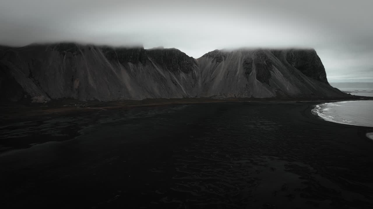воздушный черный песчаный пляж stokksnes, вулканические темные горы, vestrahorn на расстоянии, темный капризный облачный пейзаж исландия