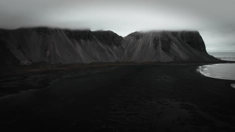 aerial black sand beach stokksnes, volcanic dark mountains, vestrahorn in distance, dark moody cloudy scenery iceland